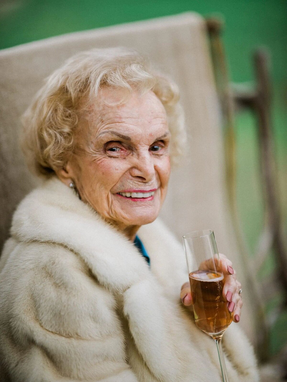 An older woman smiling and holding a drink.
