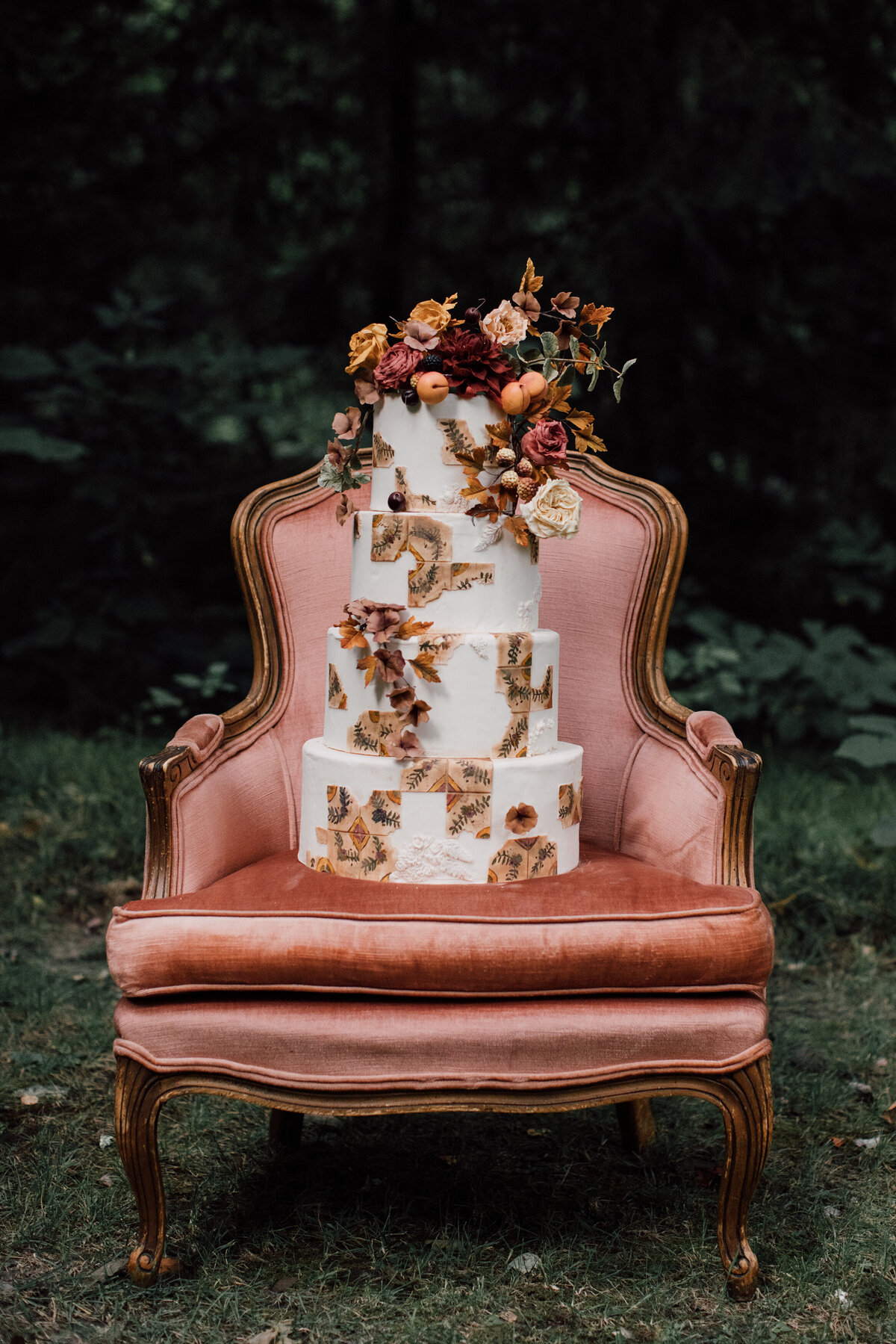 Four tiered bohemian wedding cake by Mamie Brougitte sitting on a peach velvet chair