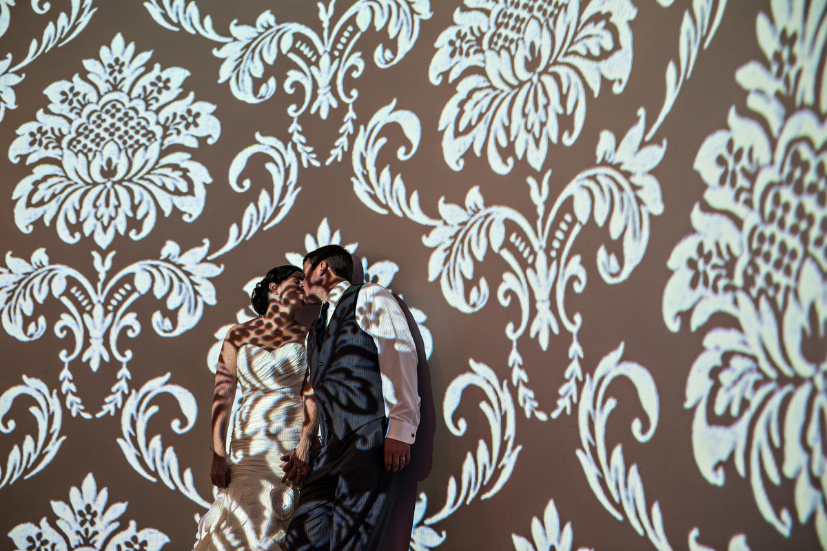 A couple kiss in the light on the wall at their Vie Wedding in Philly.