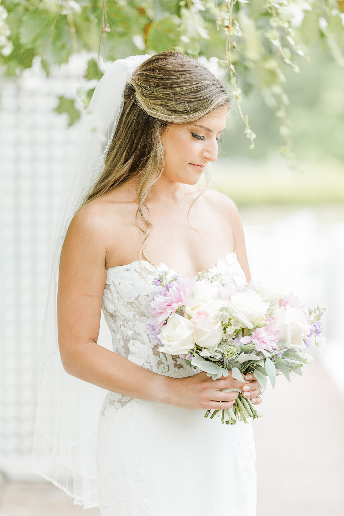 A bride poses for a formal wedding day portrait at the Five Bridge Inn. The bridge is standing angled away from the camera, she is holding her bouquet in front of her and looking down at the flowers. Captured by MA wedding photographer Lia Rose Weddings