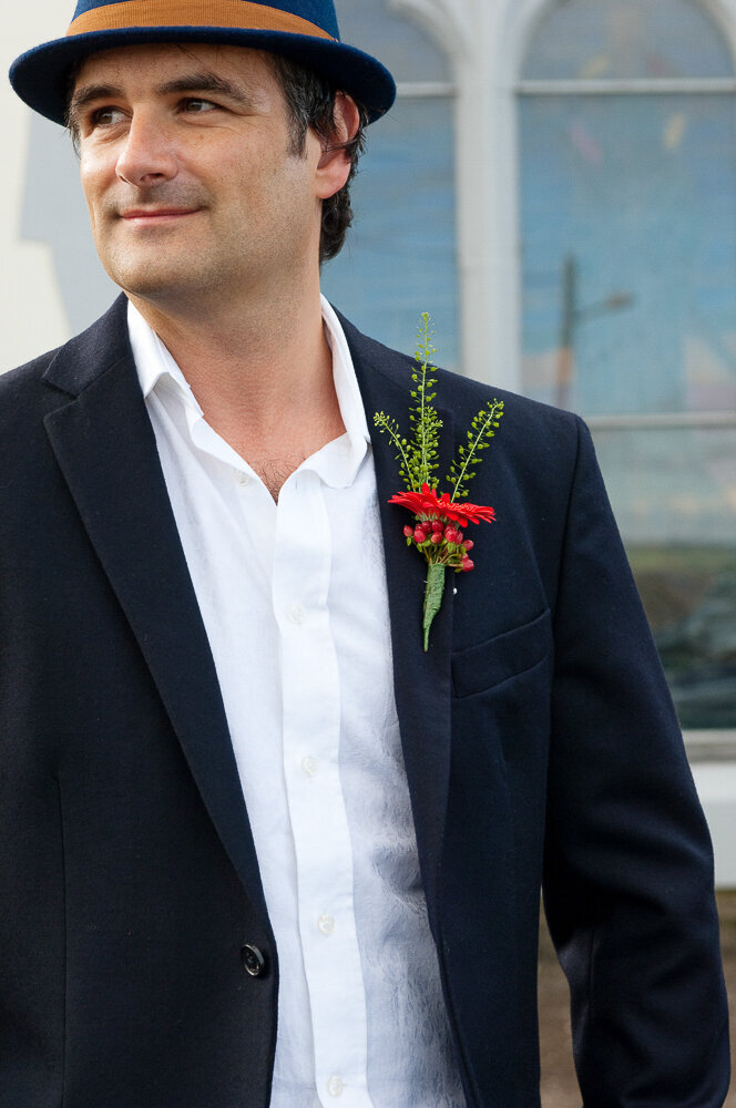 groom wearing a dark navy wedding suit and red buttonhole flower with a navy trilby hat with tan band