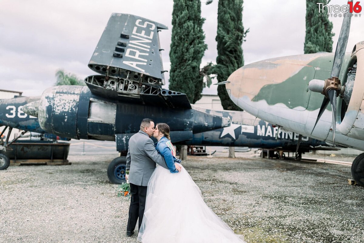 With a vintage war plane behind them the Bride and Groom share a kiss