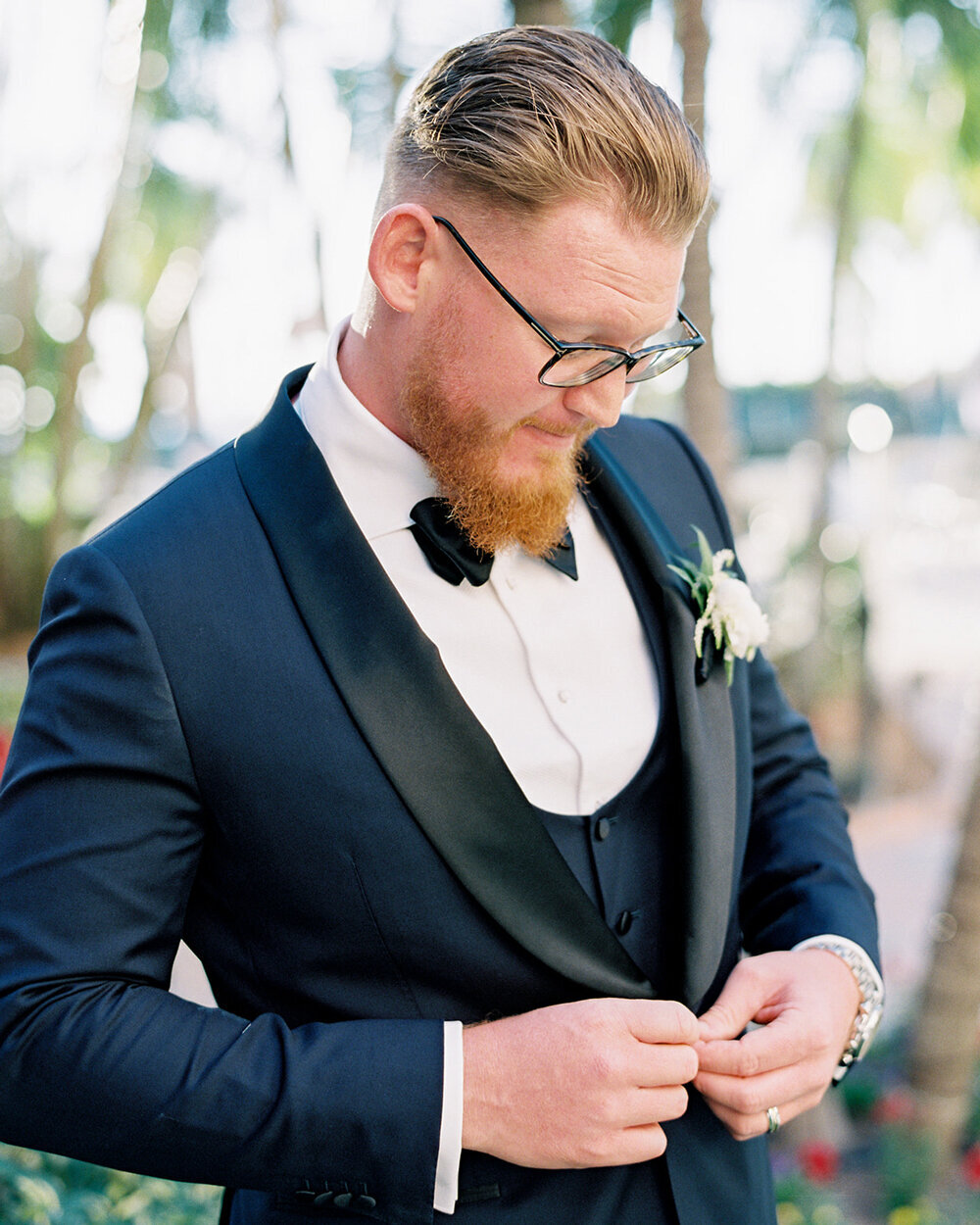 Groom buttoning his navy blue suit jacket at Don Cesar Hotel in St. Pete Beach, FL, for his December wedding.