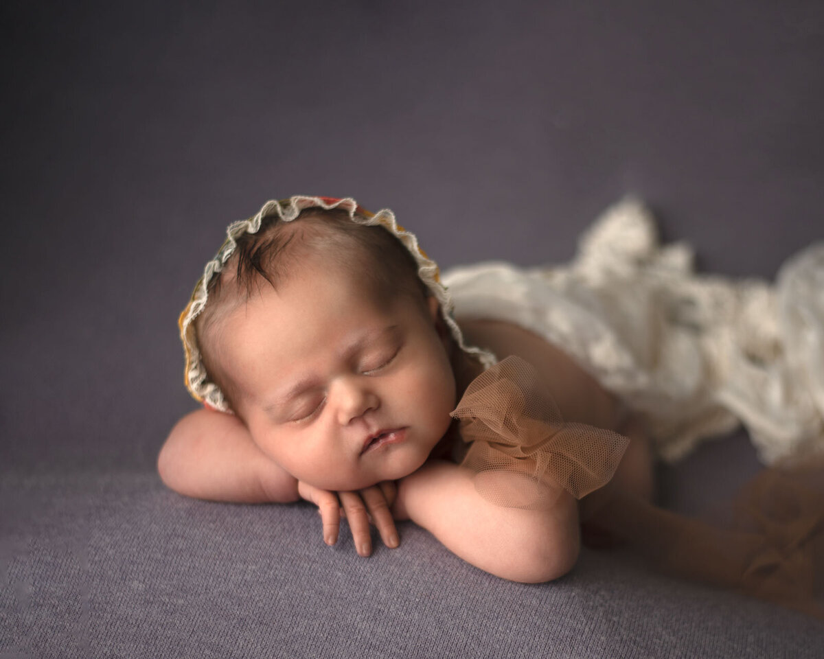 baby laying on arms with bonnet on and laying on a  purple blanket at newborn photo session