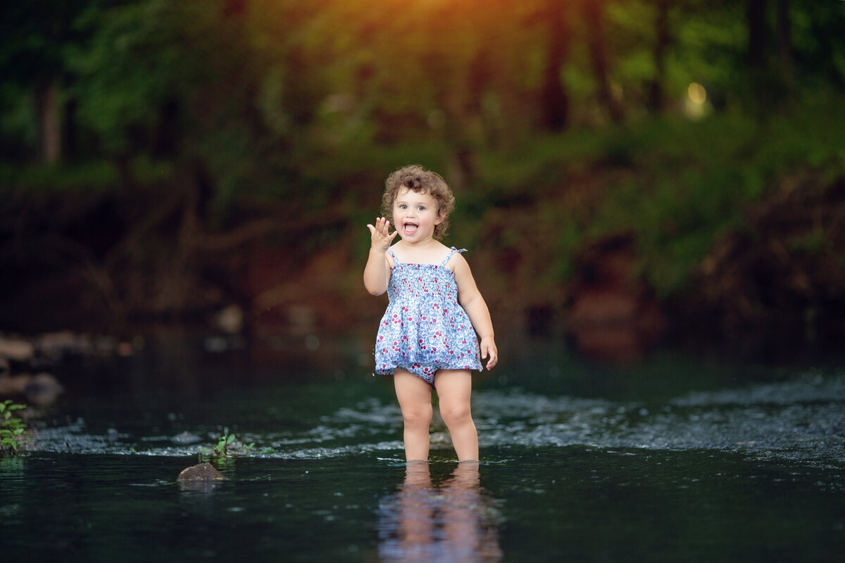 A toddler girl in a blue swimsuit plays in a shallow river at sunsetNew Jersey Family Photographer