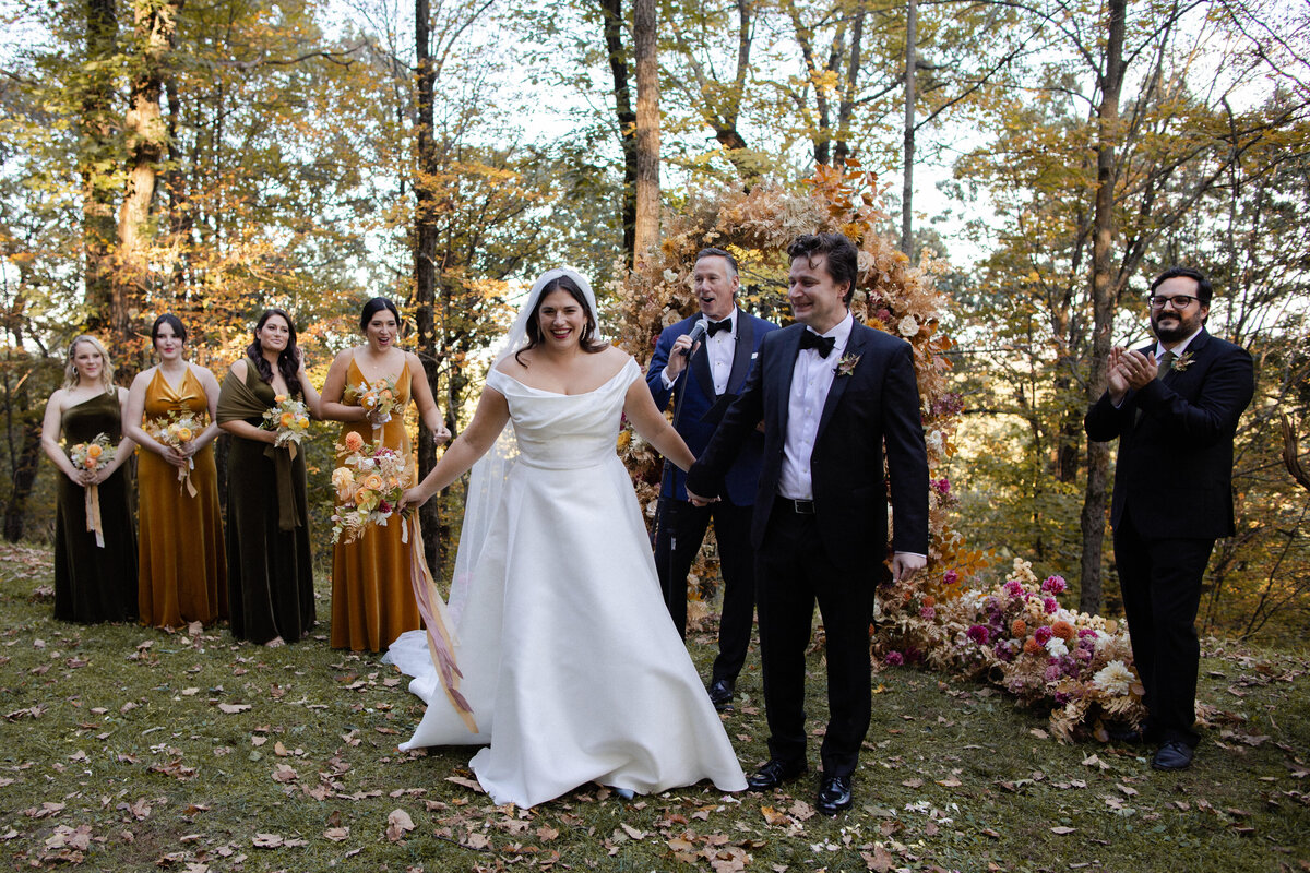 Woodsy autumn wedding with bride and groom in front of wedding party wearing a variety of brown and amber-toned dresses in Catskills