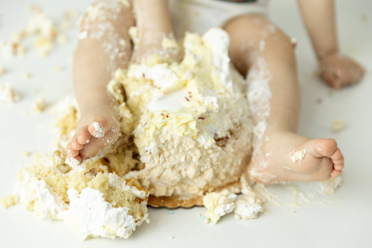 Details of a toddler feet and hands smashing a cake in a studio