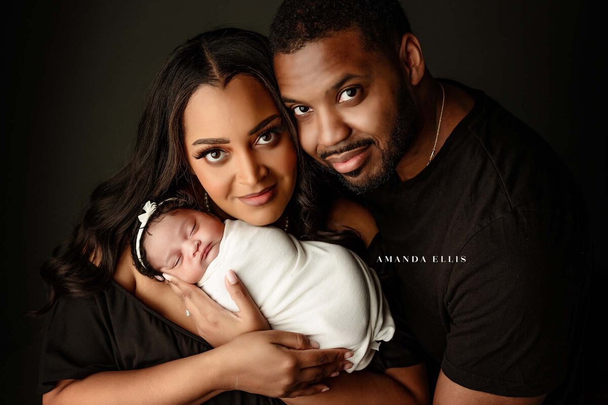 Dark luxurious portrait of family and newborn smiling into the camera