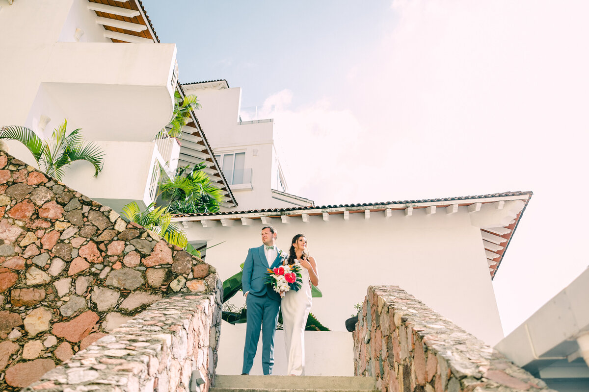 A bride and groom holding hands and flowers as they descend outdoor stone steps, captured by a Destination Wedding Photographer.