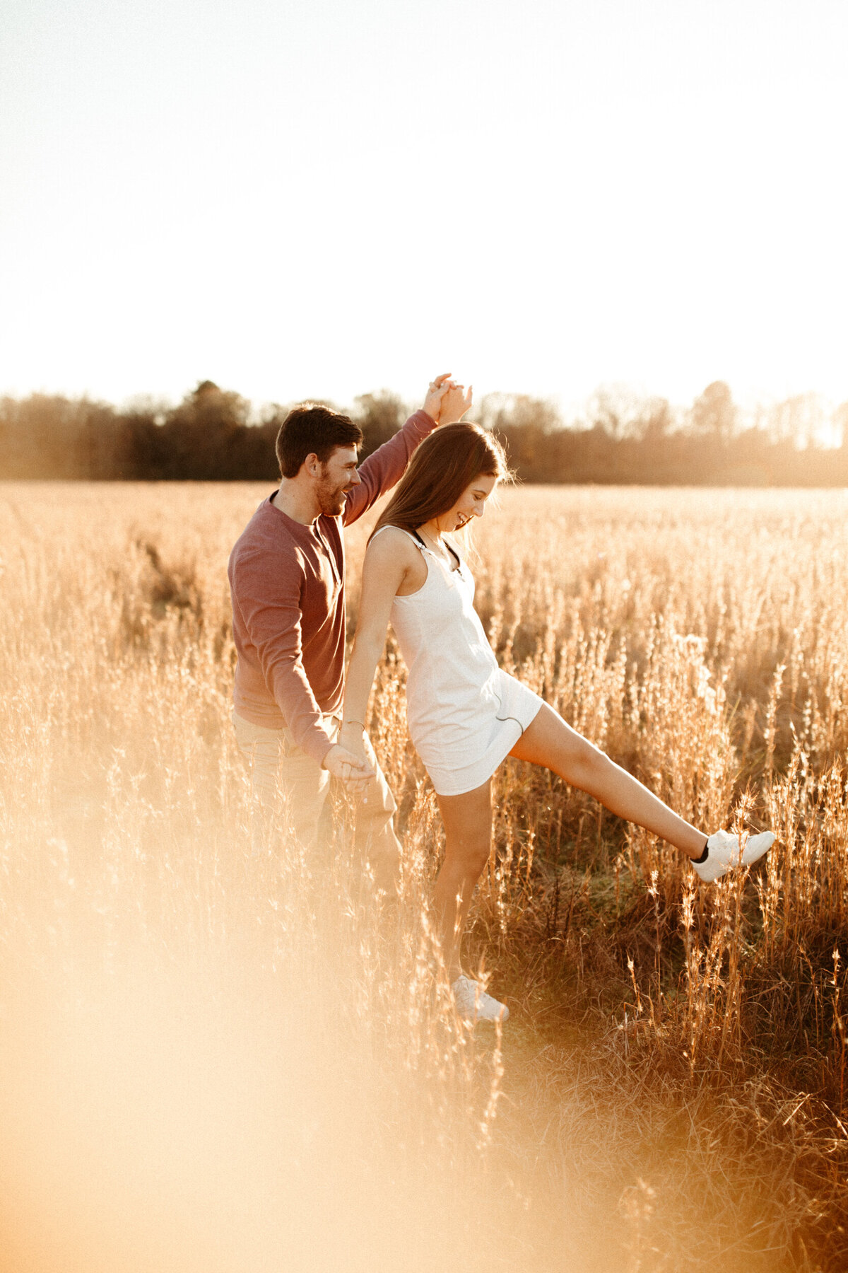 A couple is doing the airplane walk in a golden field with tall grass at sunset.