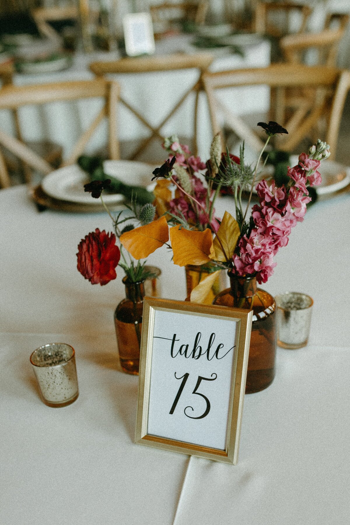 Elegant wedding table setting at Park Farm Winery featuring a floral centerpiece and a gold-framed table number 15 sign, with candles and wooden chairs in the background.
