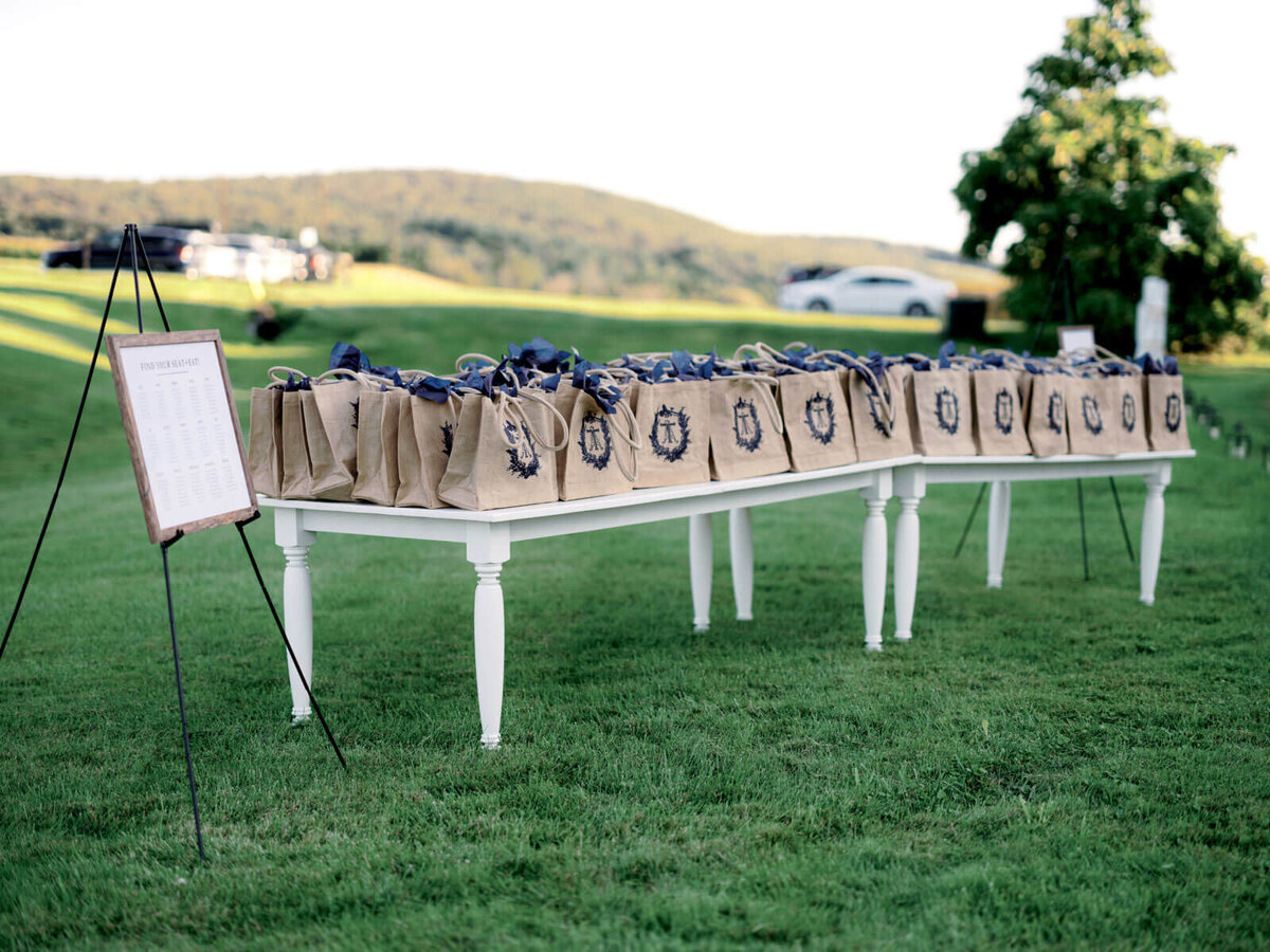 A long table outdoors filled with wedding give-away little brown bags at Lion Rock Farms, CT. Image by Jenny Fu Studio