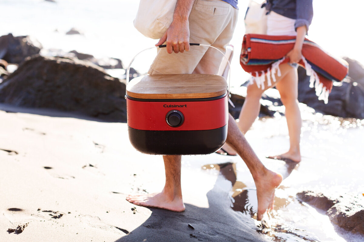 People walking on the beach and carrying cuisinart products and other picnic supplies
