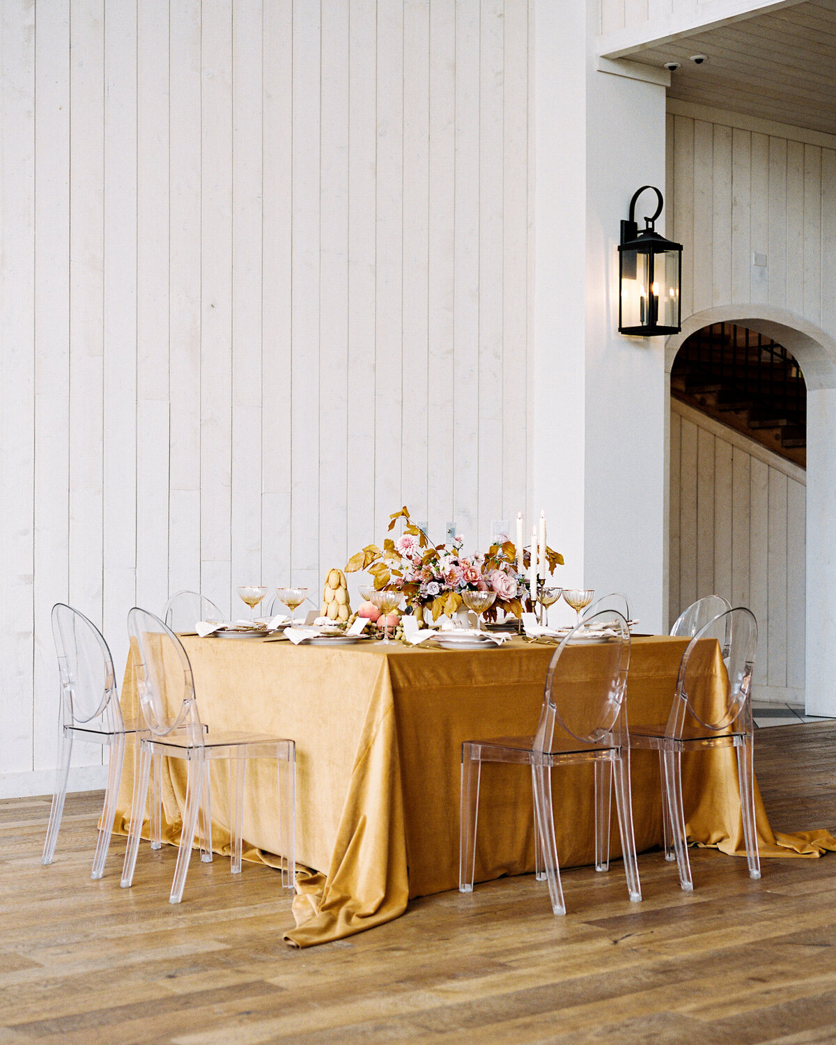 Pulled back image of romantic table setting featuring golden velvet tablecloth and modern chairs