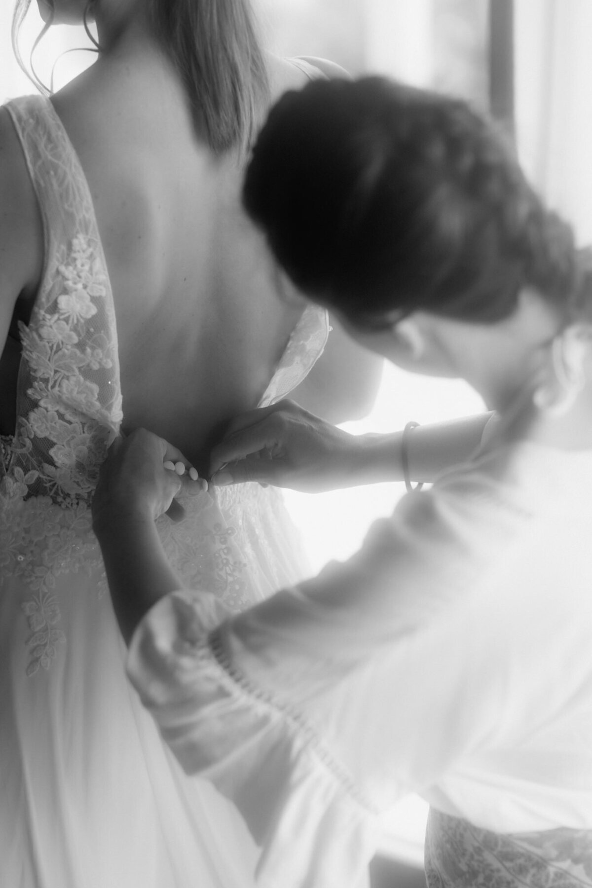 Eine Freundin hilft der Braut beim Zuknöpfen ihres Kleids.