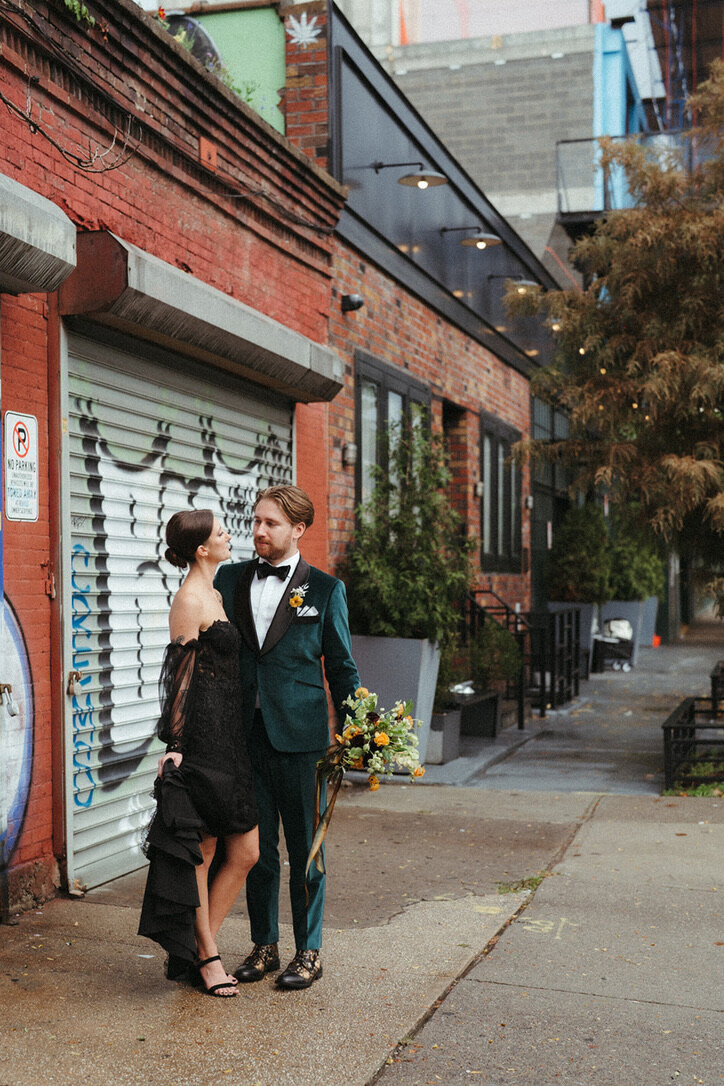 Bride wearing a black dress and low bun posing with groom in the streets of Brooklyn New York