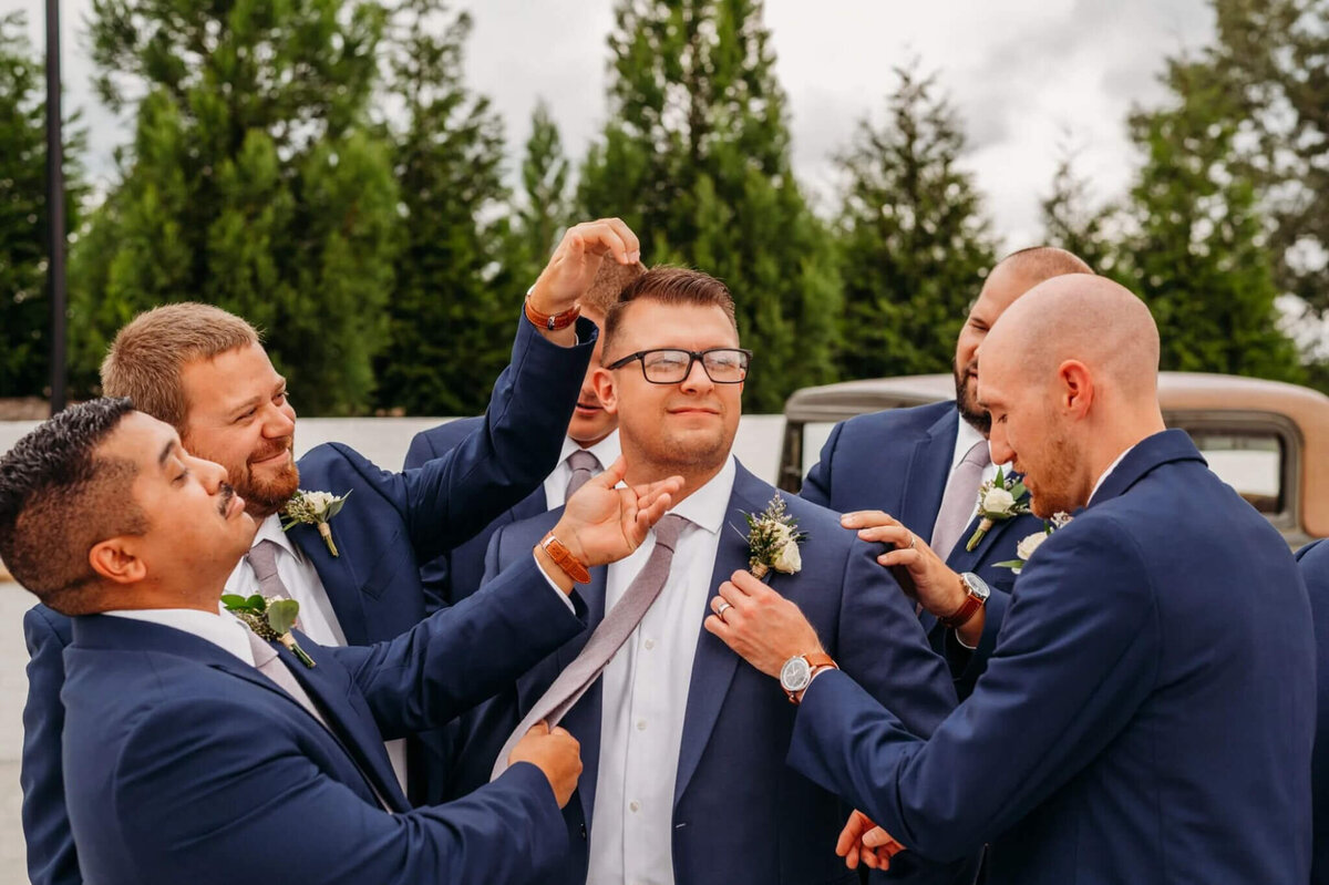 Photo of men wearing navy suits and fixing the grooms attire in a funny manner