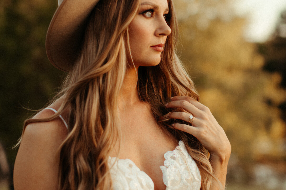 Boho bride in a wide brim hat looking off while running her fingers through her loose curls