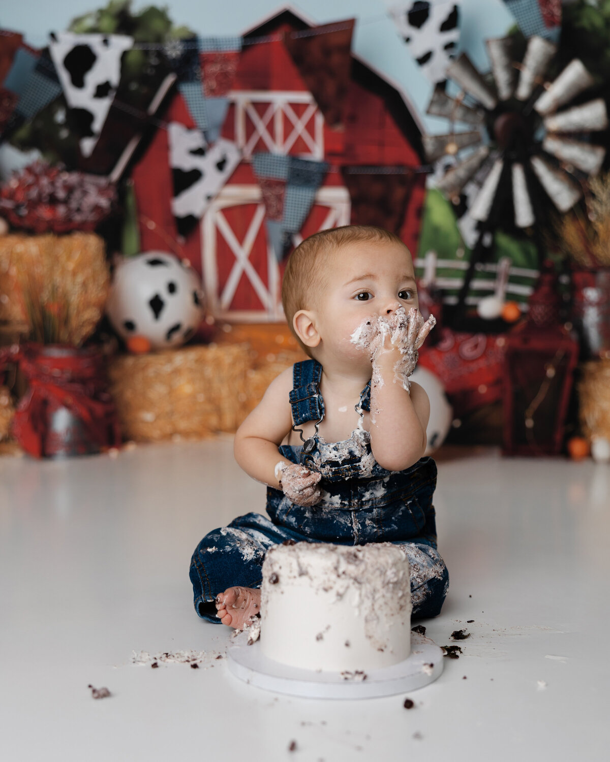Joyful first birthday moment as baby boy claps frosting-covered hands during his barnyard cake smash.
Photograph by Yucaipa cake smash photographer Kaitlyn Dawn Photography.