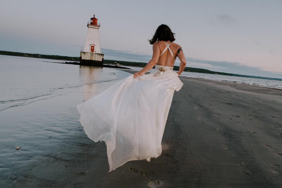 Bride running towards lighthouse at low tide in Nova Scotia.