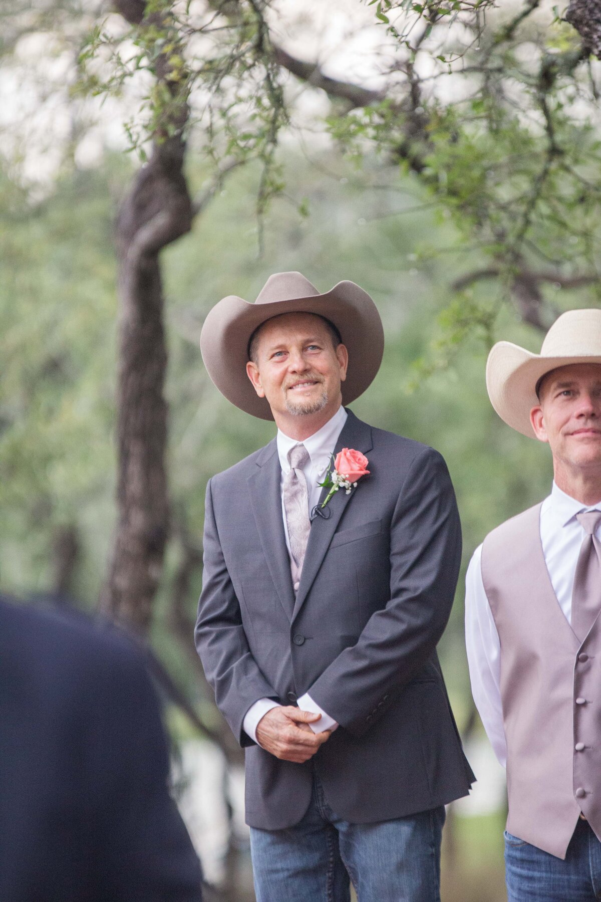 groom in cowboy hat peers through aisles to bride coming toward him in Boerne Texas wedding
