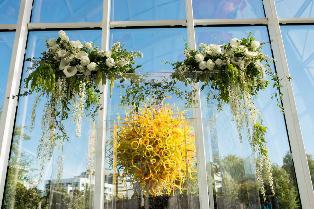 White and green floral arrangements atop the lucite wedding huppah look like they are floating.