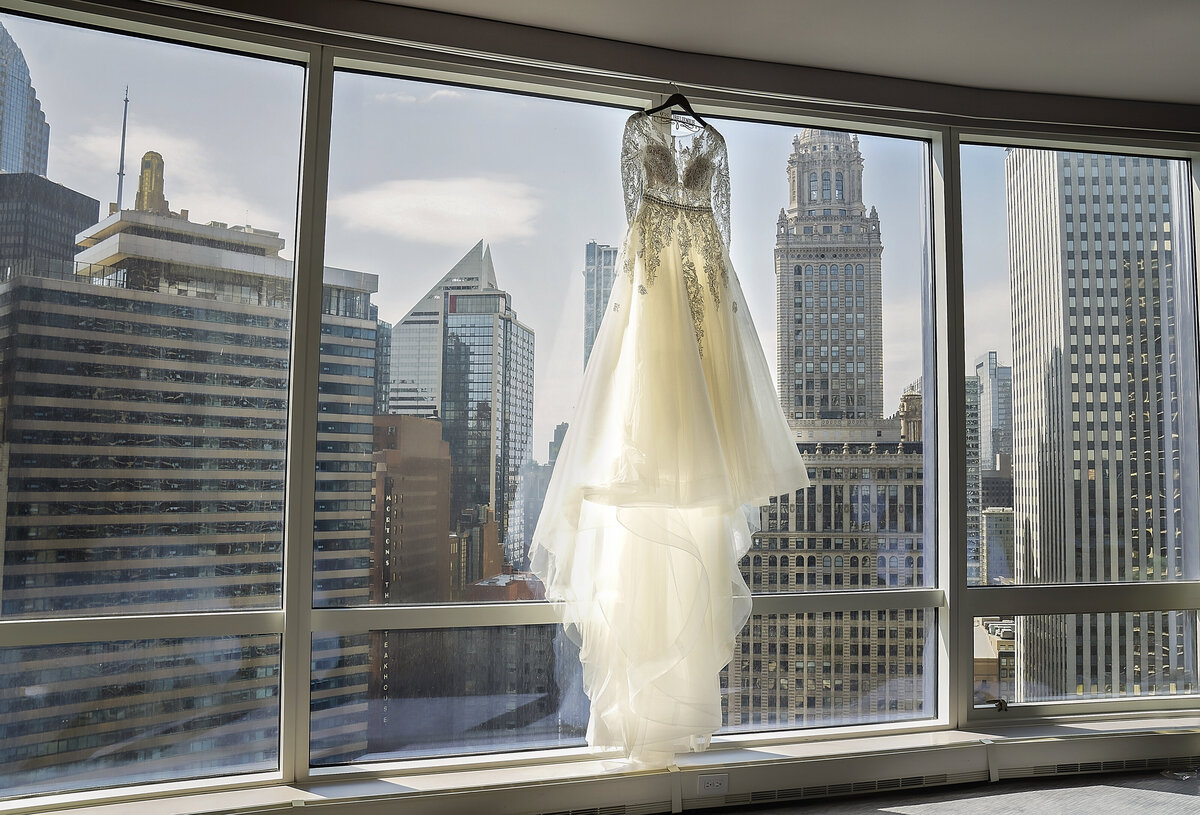 White Bride's wedding dress hanging on the huge ceiling to floor window with the view of Chicago skyscrapers