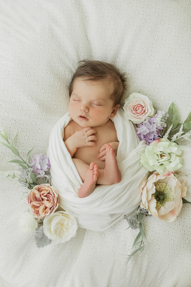 newborn baby girl swaddled with flower placed around her