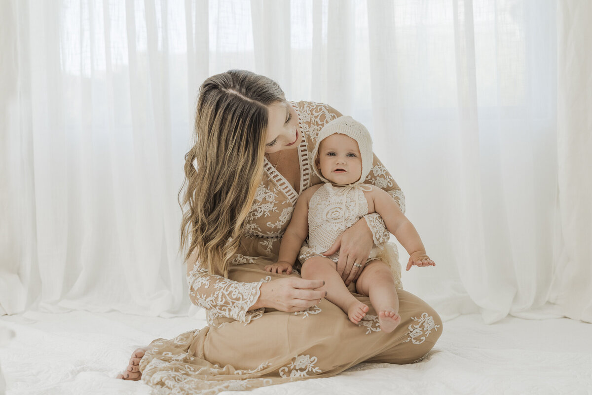 blonde woman sitting holding her baby in a beautiful taupe gown and neutral colored outfits