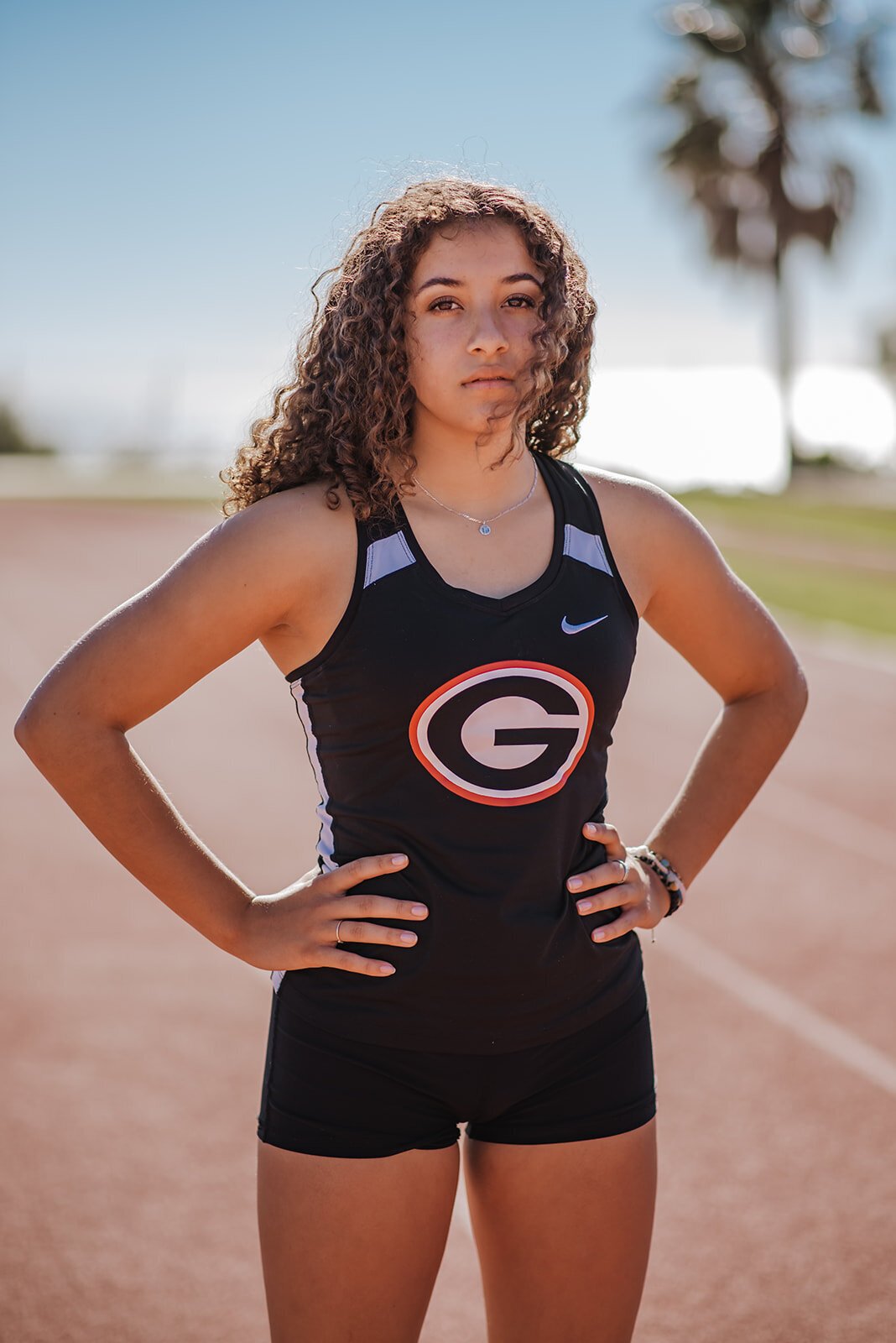 Olivia poses on a track in her running uniform for senior portraits.