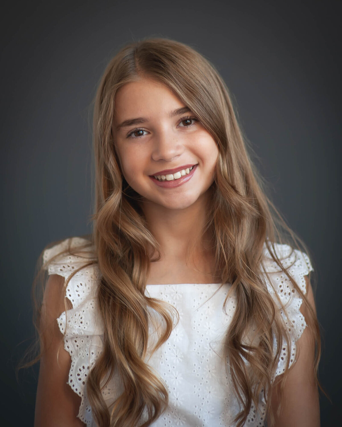Sweet 10 year old girl smiling wearing white shirt with a dark grey background