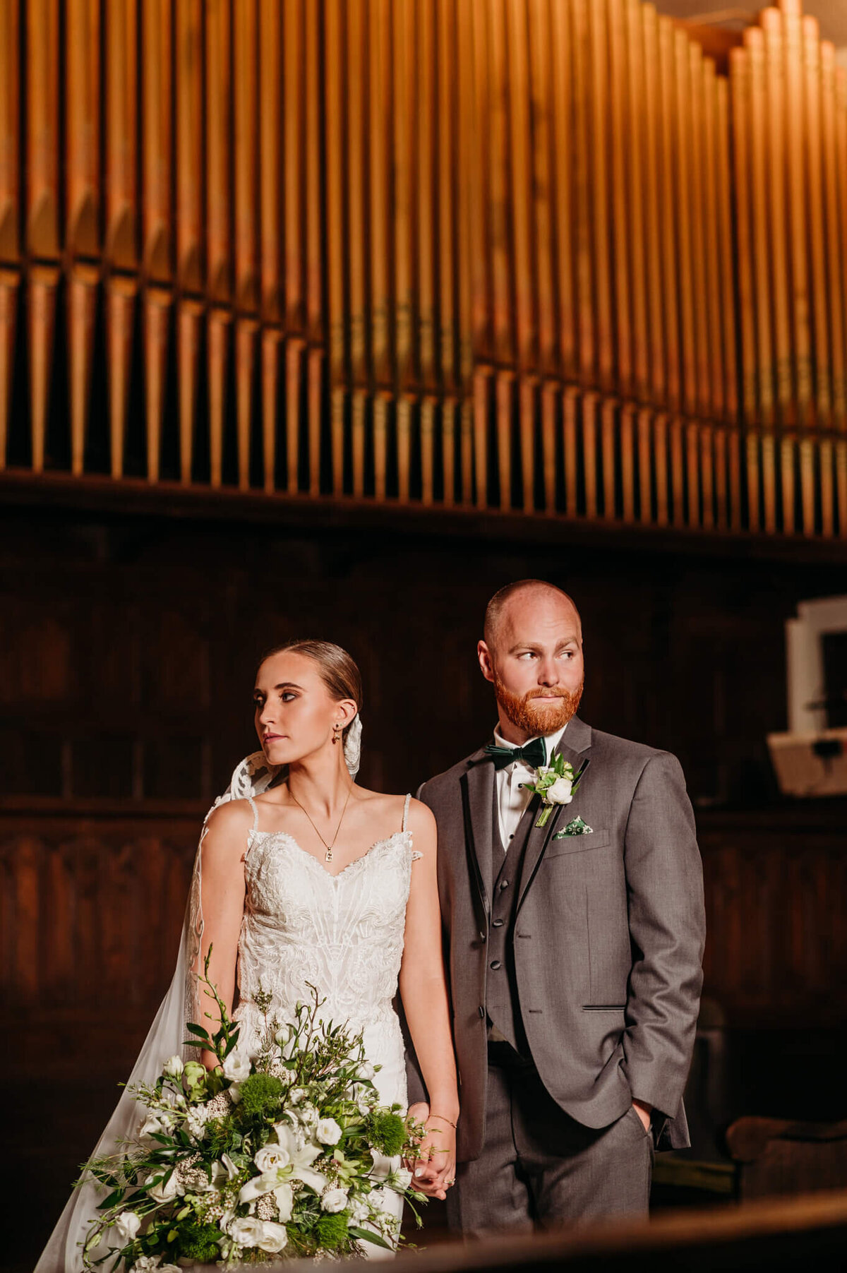 Photo of a bride and groom holding hands and looking away with an organ in the background