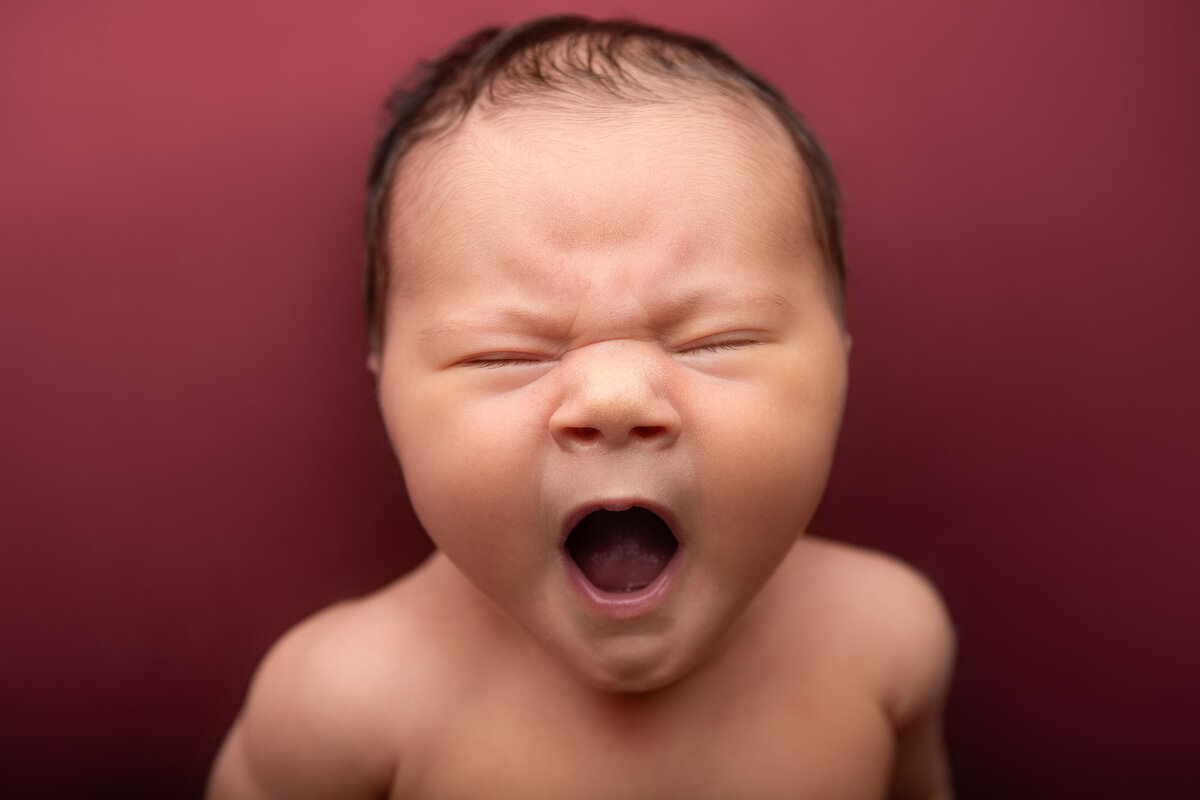 Yawning newborn pose on a red backdrop
