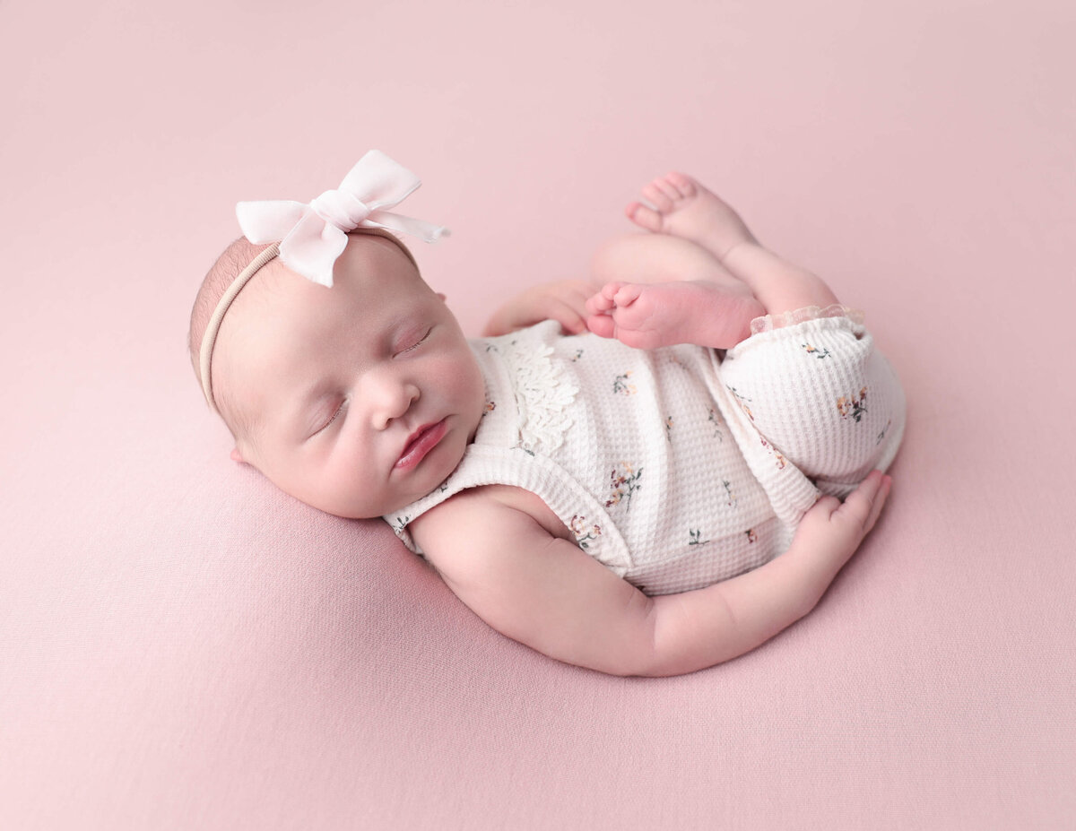 Precious baby girl posed on a pink backdrop in Rochester, Ny.