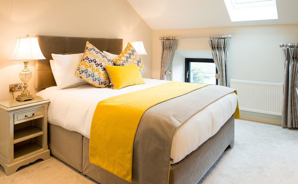 Hotel bedroom with double bed covered in yellow and grey bed linen