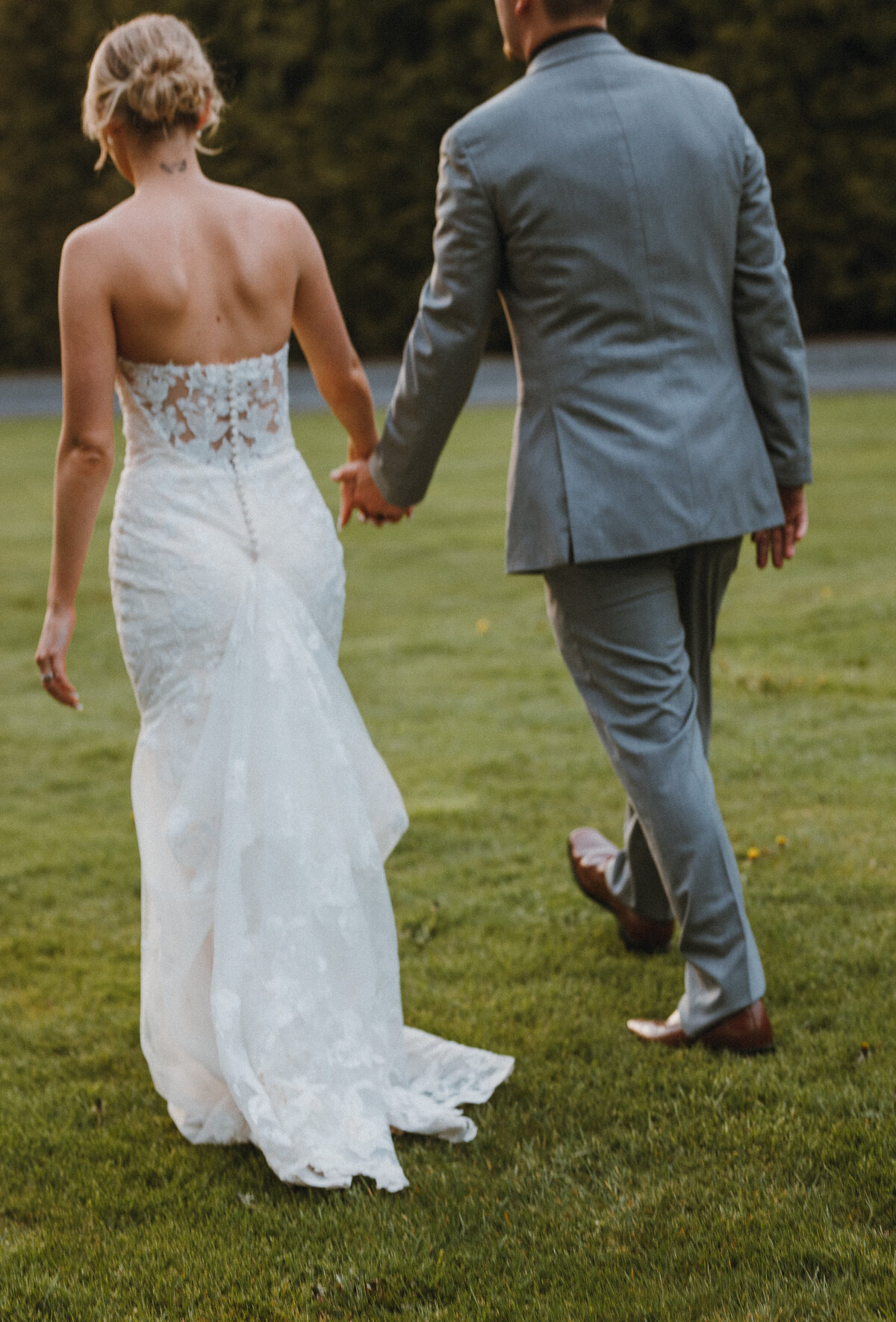 Bride and groom holding hands walking on a grassy lawn