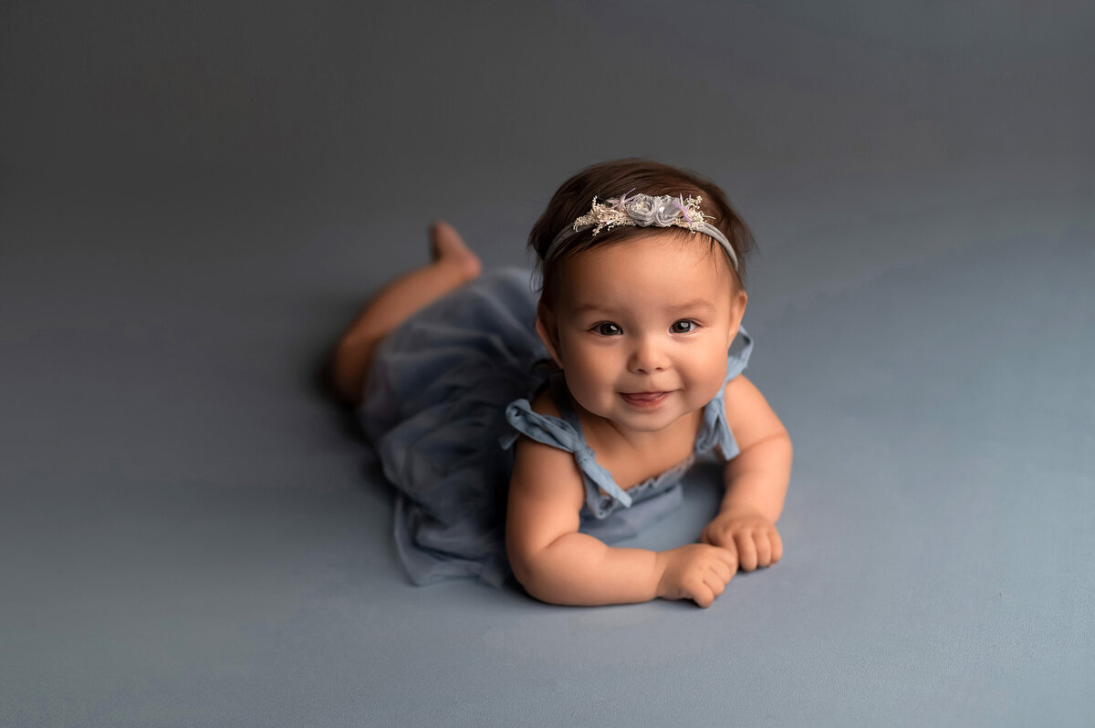 A baby girl lays on her belly in our Waukesha photo studio and gives a sweet smile to the camera.