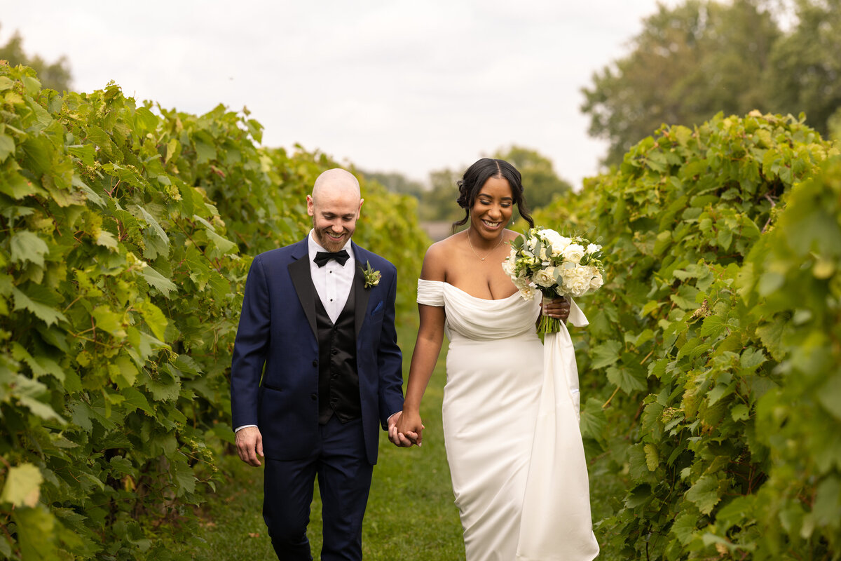 Groom and bride happily walk down the aisles of a vineyard. Photo taken by Aaron Aldhizer