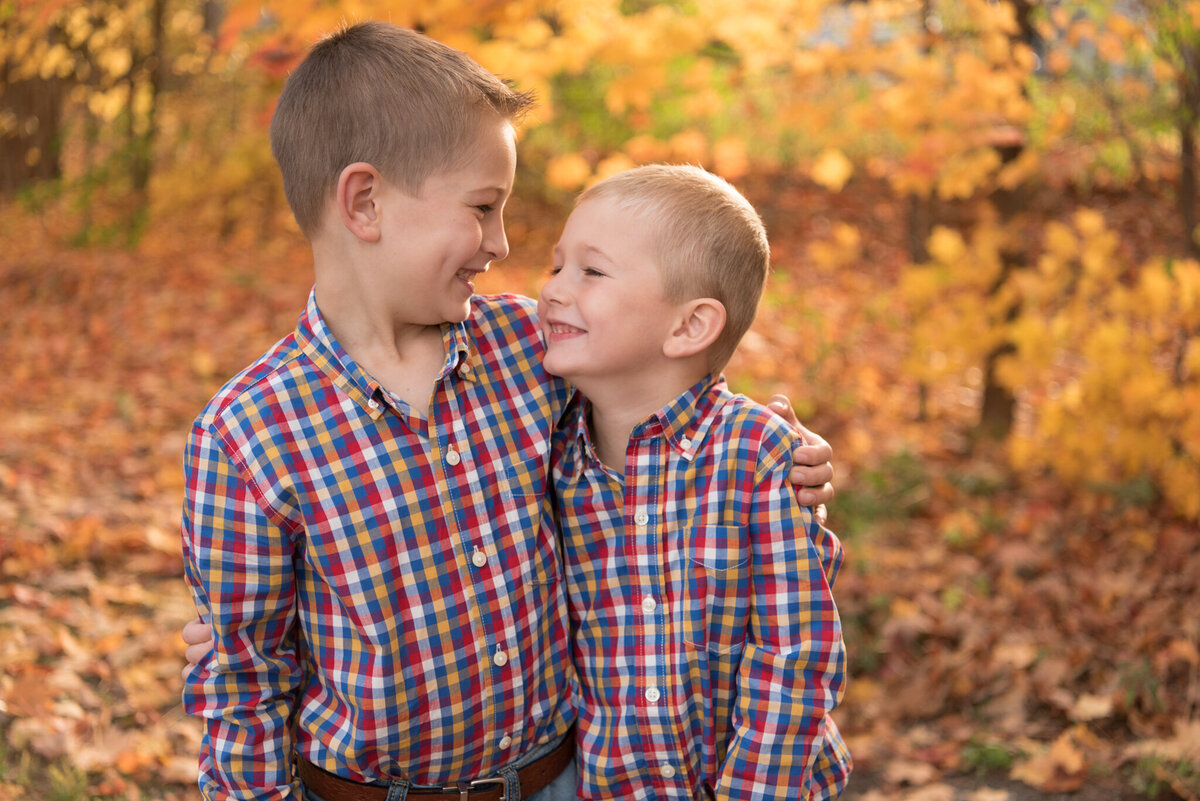 Two young brothers smiling at one another with orange leaves behind them