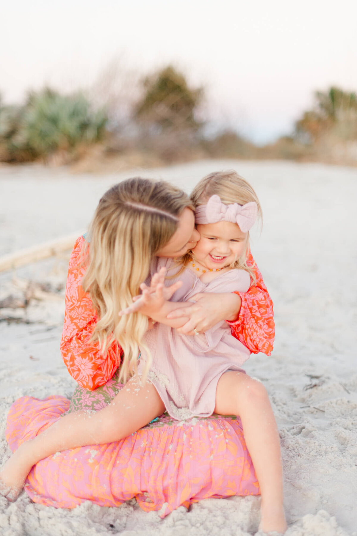Mom kissing daughter while she laughs and plays in the sand