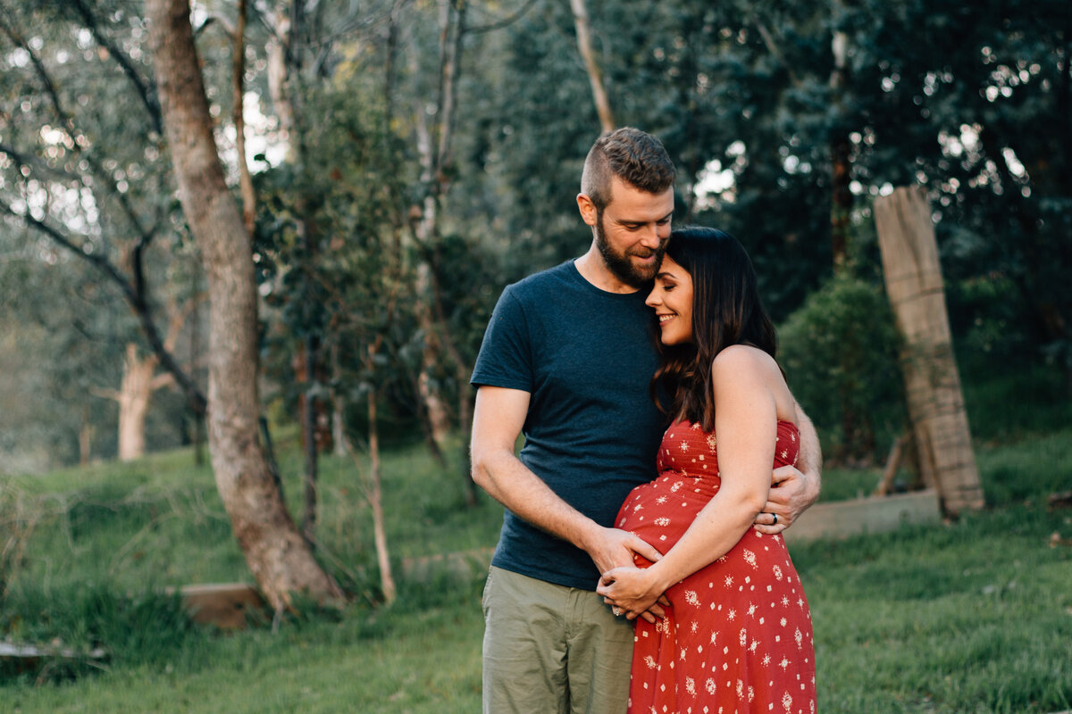 Couple embracing outside with hands on pregnant belly, taken during Melbourne maternity photography session