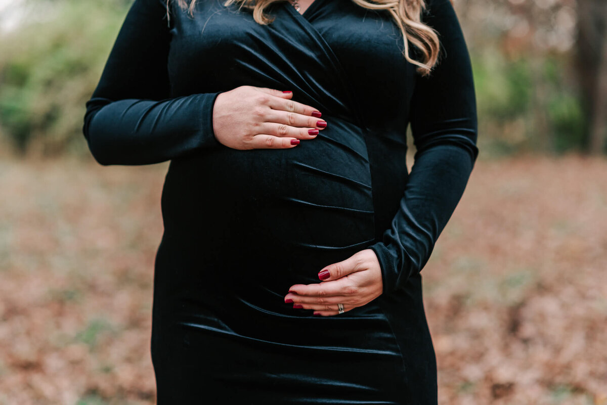 A closeup of a woman with arms circling her bump, at Lake Fairfax Park in Northern Virginia