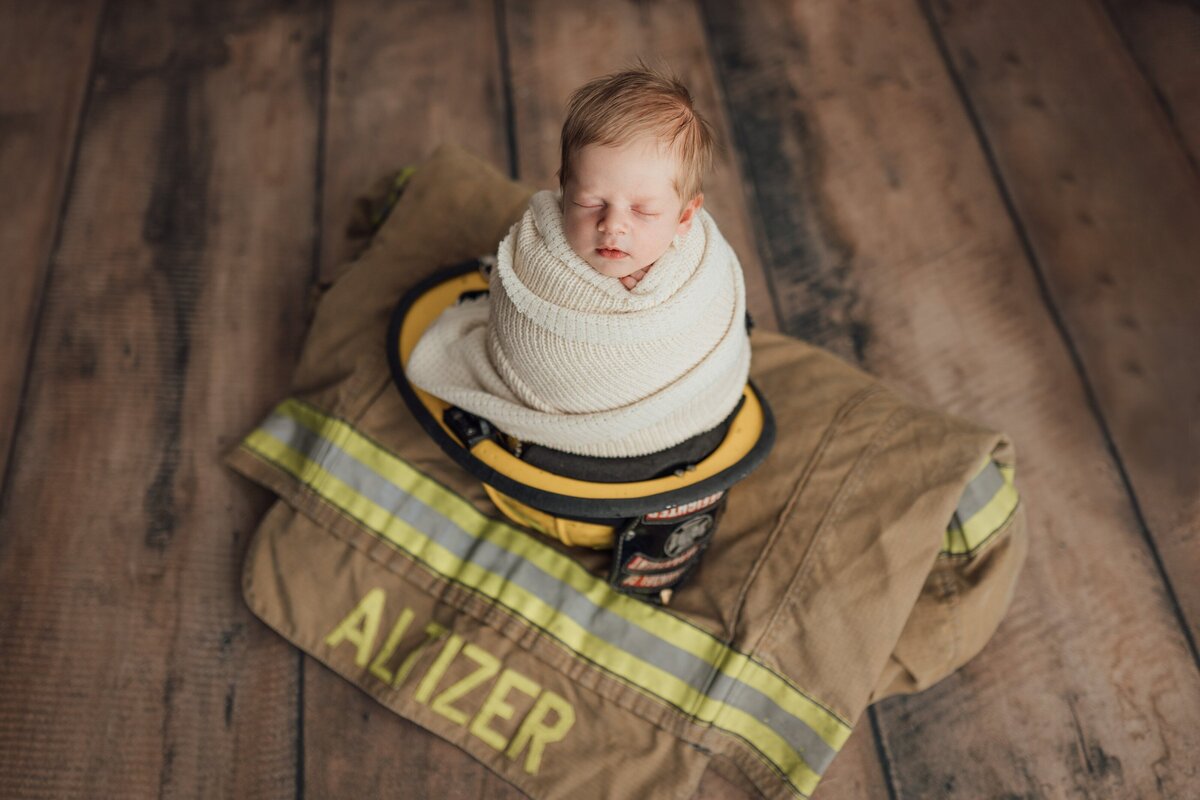 newborn baby poses on dad's fire hat during studio newborn session in land o lakes