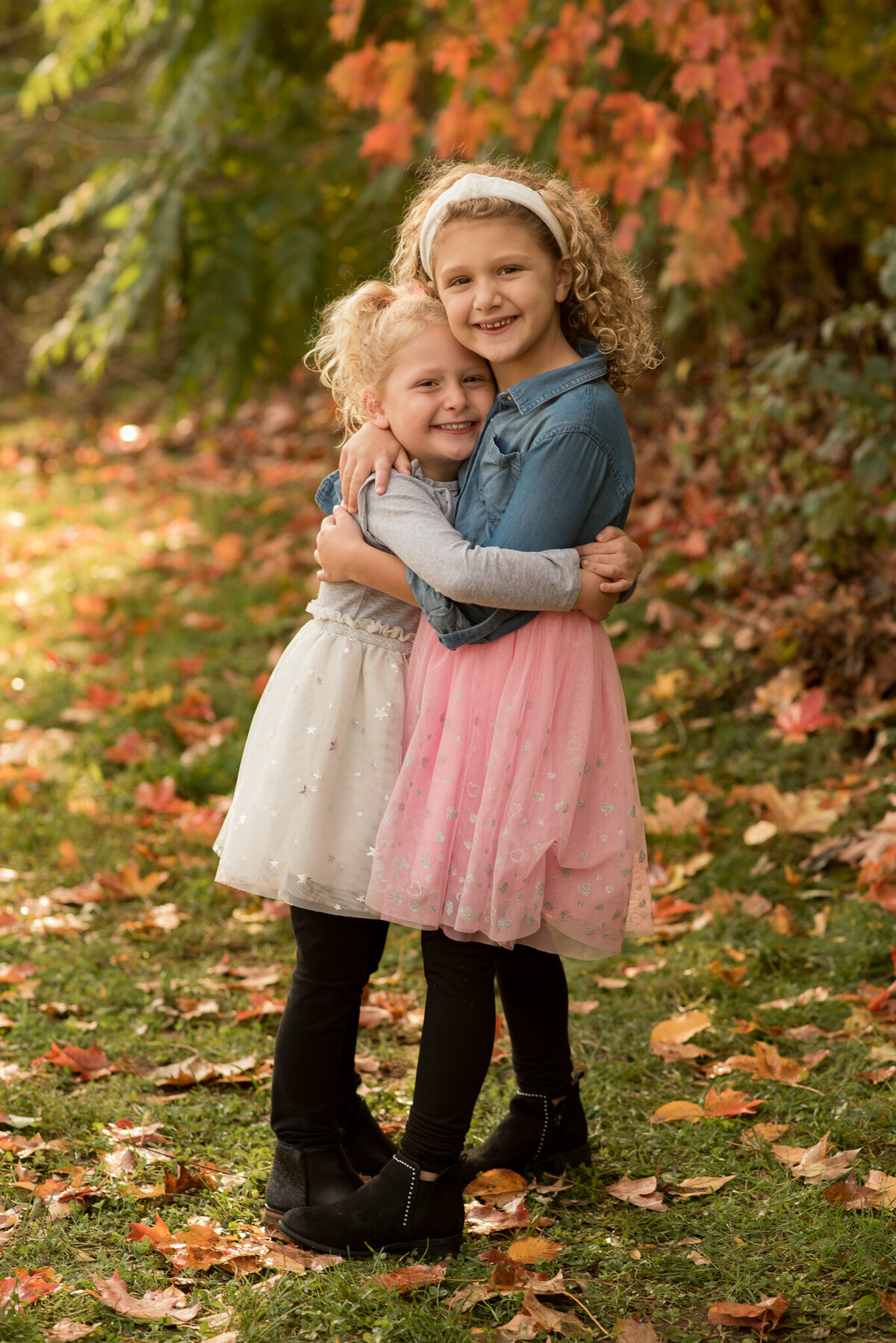 Two sisters hugging each other with fall leaves in the background