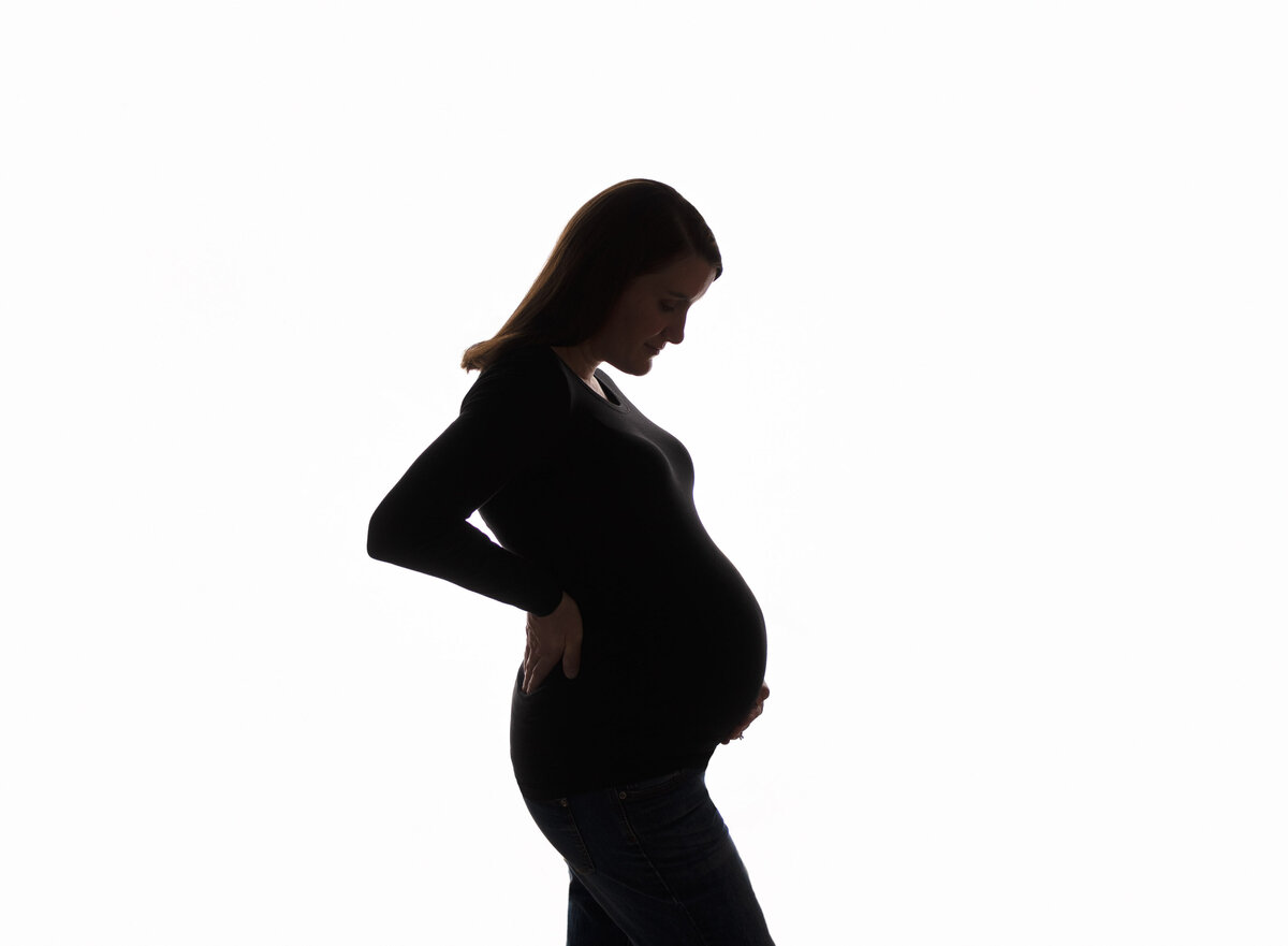 Silhouette of expectant mother looking down at her baby bump