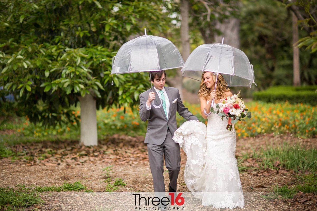 Bride and Groom go for a walk a the Fullerton Arboretum under clear umbrellas because of the light rain