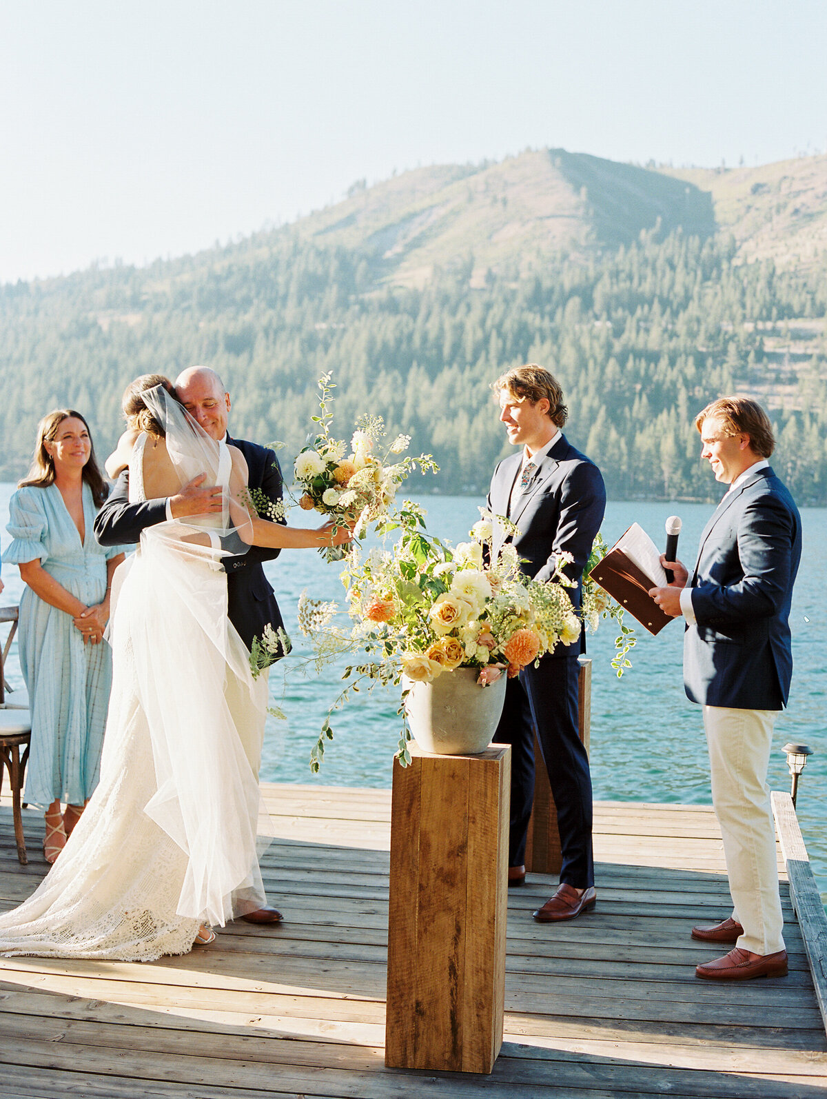 photo of ceremony on family dock on lake tahoe with brides father giving her a hug at the end of the aisle before she gets married
