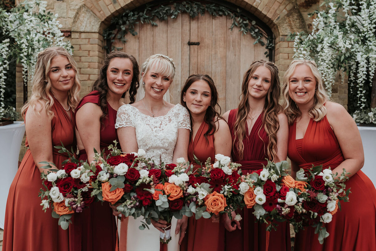 Bride and Bridesmaids wearing burgundy & orange satin dresses holding gorgeous autumnal wedding bouquets at The Ravenswood