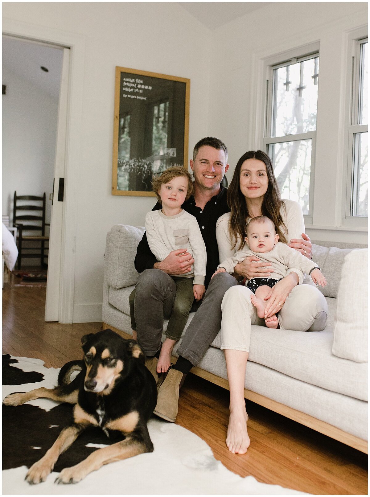 Posed photo of family sitting on sofa with toddler and baby and dog lying on rug at sweet home family session in Austin by Amber Vickey Photography