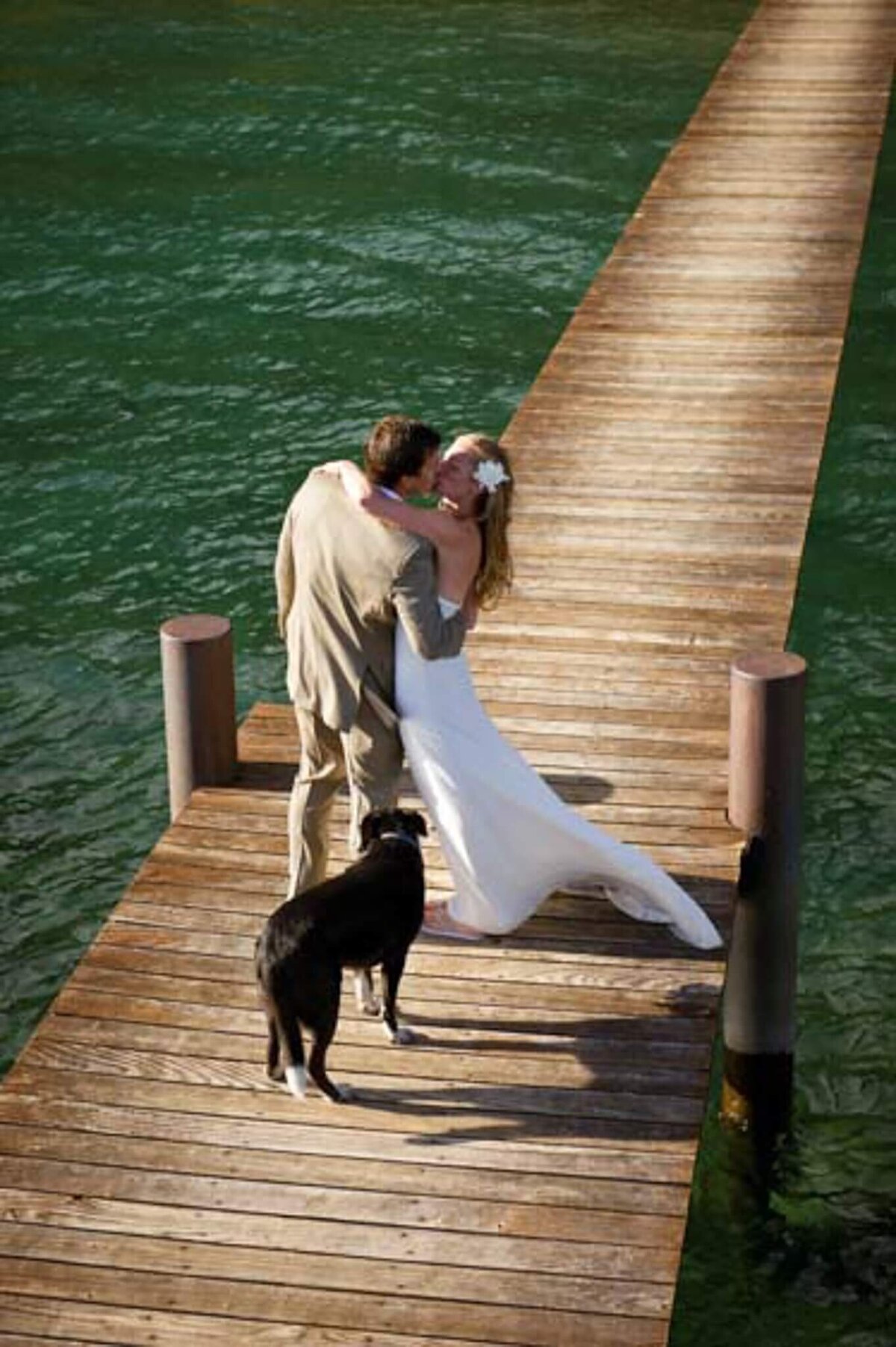 couple kissing on a pier in Lake Tahoe with their dog in tow